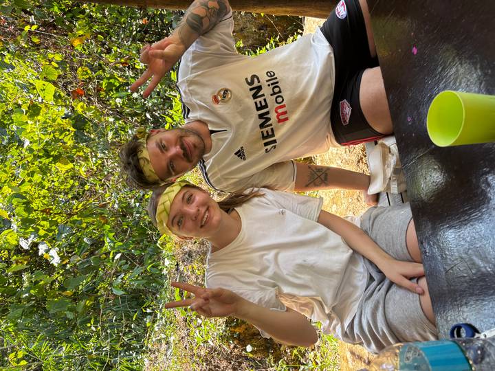 Two young travellers wearing leaf headbands smiling and giving peace signs at an outdoor table.