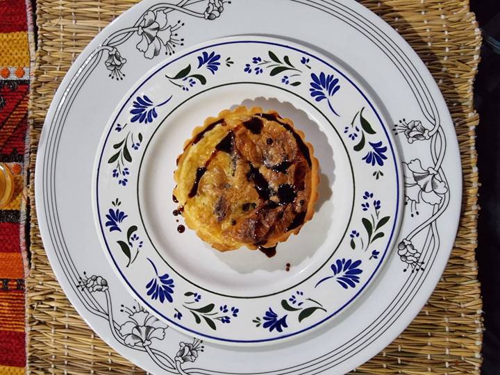 Close-up of small Moroccan-style savory tart drizzled with dark sauce on decorated ceramic plate.