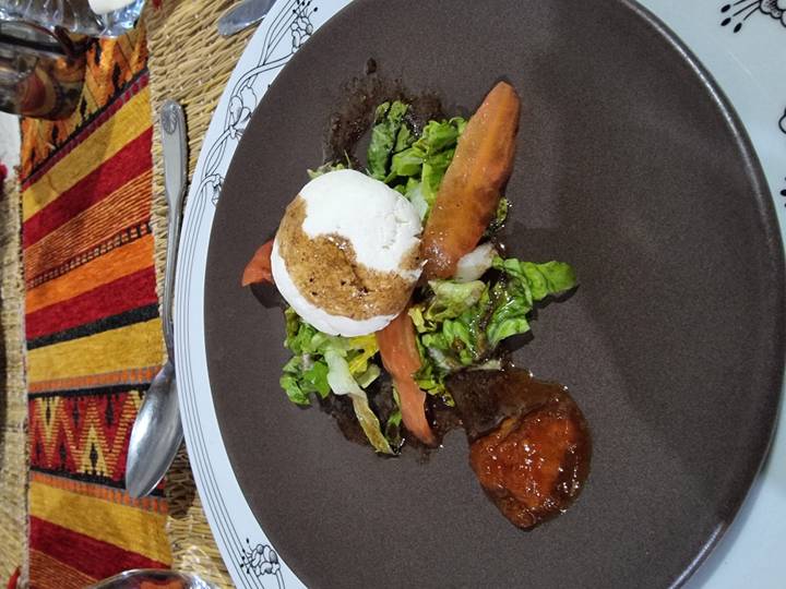 Close-up of a plated salad topped with a soft cheese ball and dressing, on a restaurant table with colorful woven placemat.