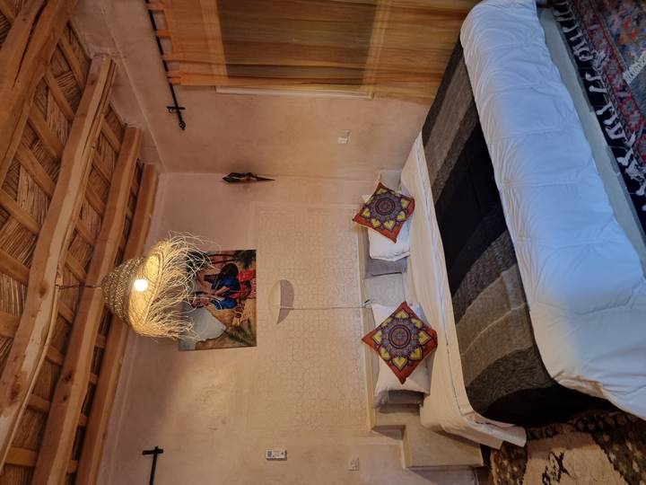 Cozy guest-room with a double bed, colorful Moroccan cushions, woven ceiling, and soft ambient lighting.