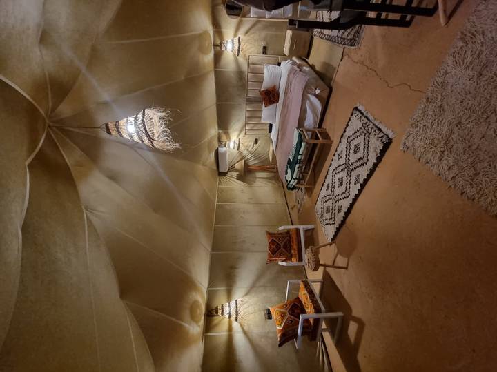 Spacious desert glamping tent with a neatly made bed, woven lanterns, and rustic furnishings.