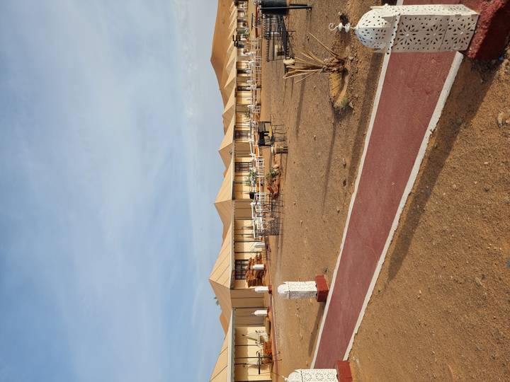 Row of beige luxury tents set on desert sands with low dune backdrop and clear sky.