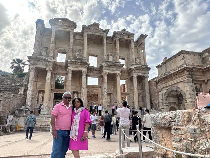 Couple posing in front of ancient marble Library of Celsus with tourists milling around