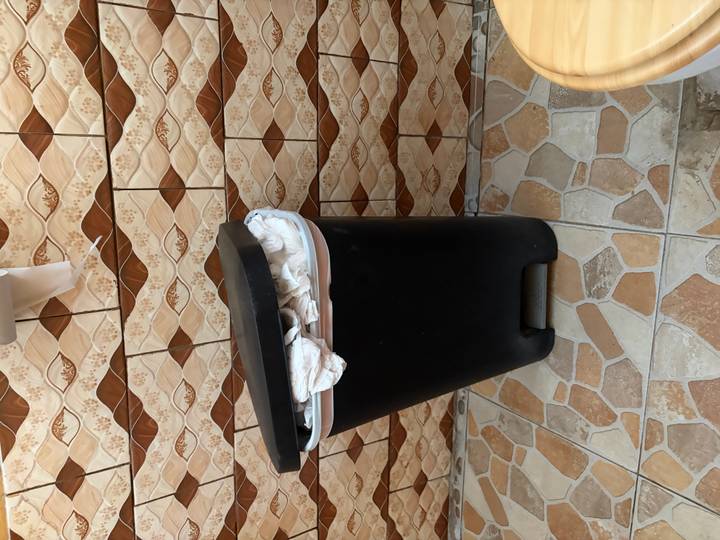 Indoor photo of an overflowing black trash bin against patterned tiles