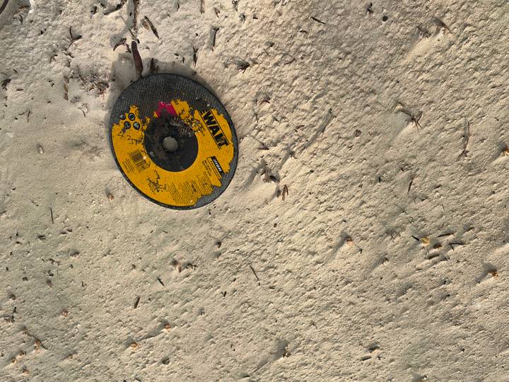 A damaged circular saw disc lying partially buried in light sand