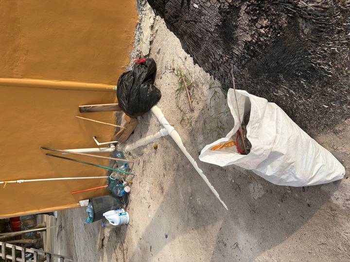 Outdoor pile of rubbish, pipes and plastic bottles beside a yellow wall
