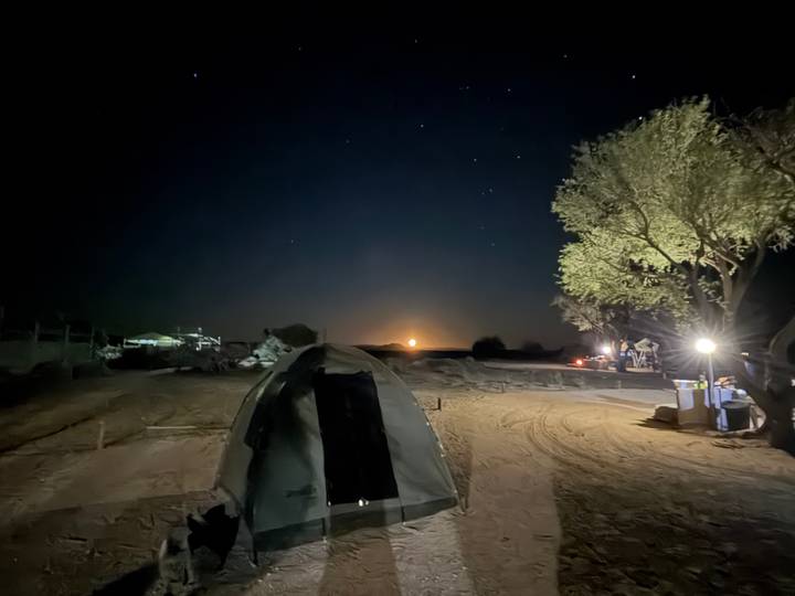 Night campsite scene with a single pitched tent, sandy ground and a bright moon or rising sun on the horizon.
