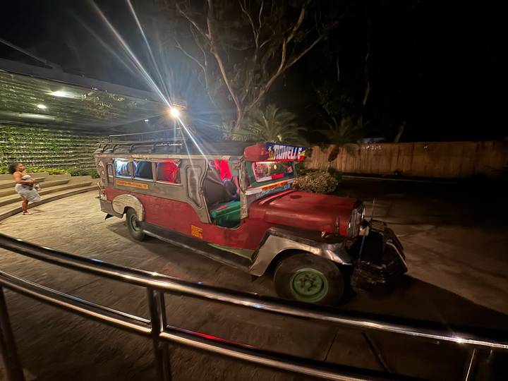 Colorful Philippine jeepney parked at night under dim lighting with a passer-by nearby.