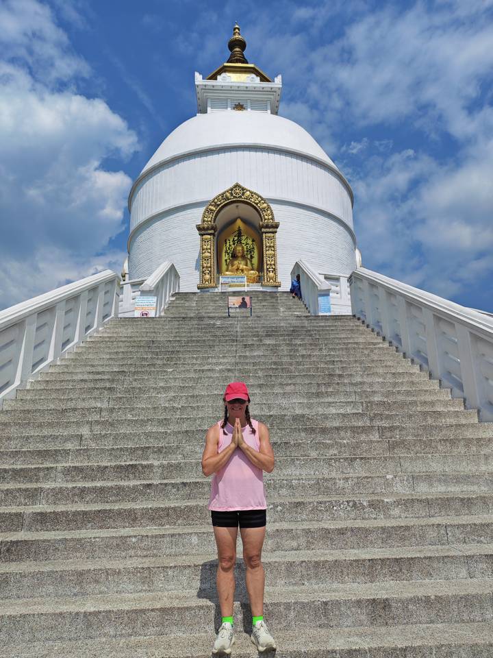 A visitor stands on broad stone steps in prayer pose before the gilded Buddha of the World Peace Pagoda.