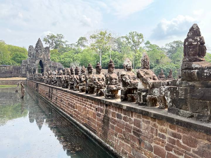 Rows of weathered guardian statues line the sandstone bridge leading to Angkor Thom’s gate, reflected in the moat below.