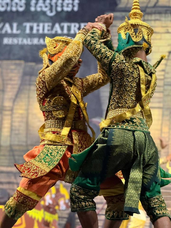 Two elaborately costumed Cambodian dancers perform a traditional routine, motion blur visible on their ornate attire.