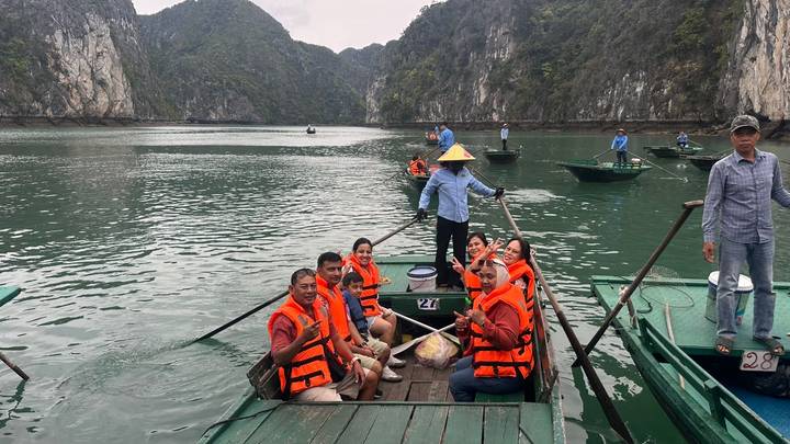 Tourists in orange life vests sit in wooden rowing boats amid limestone karsts of Ha Long Bay.
