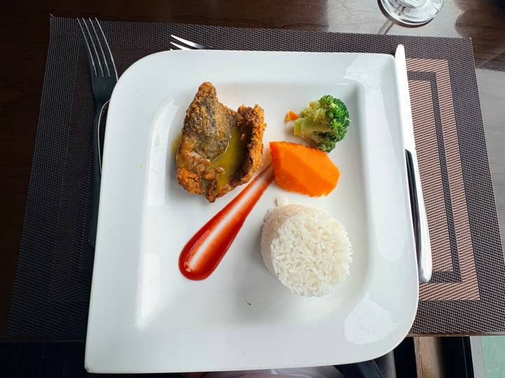Minimalist presentation of fried fish, vegetables and rice on a square white plate.