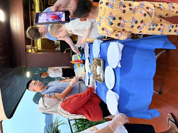 Small cooking class on a boat deck where travellers and children prepare food together.