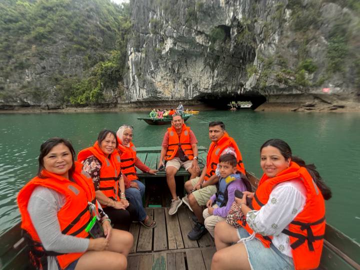 Smiling group wearing life jackets in a small boat near a karst cave entrance in Ha Long Bay.