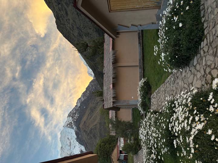 Stone pathway through daisy gardens leads to cosy lodges framed by sunset-lit Andean peaks.