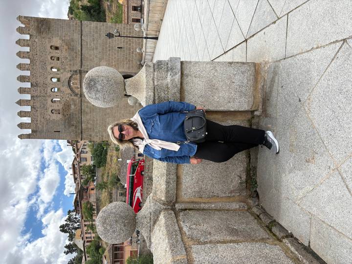 Visitor leans against a granite balustrade on a medieval stone bridge with fortress walls behind.