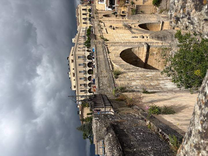 Dramatic arched bridge spans a deep gorge below stormy skies with historic Ronda buildings lining the edge.
