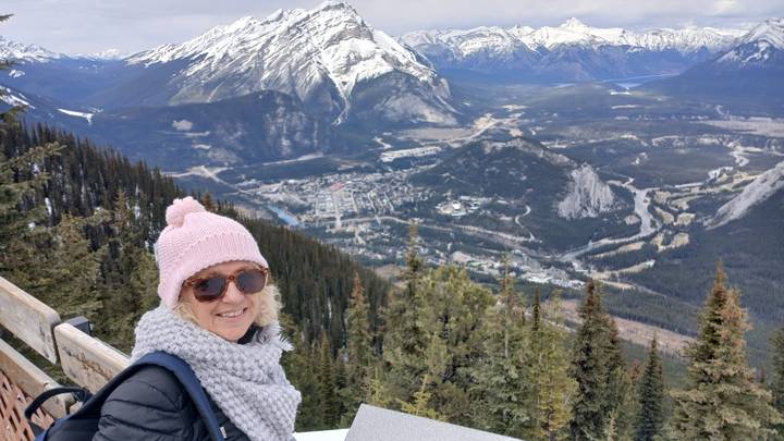 Traveller bundled in winter gear enjoys a panoramic mountain view over Banff townsite from a lookout.