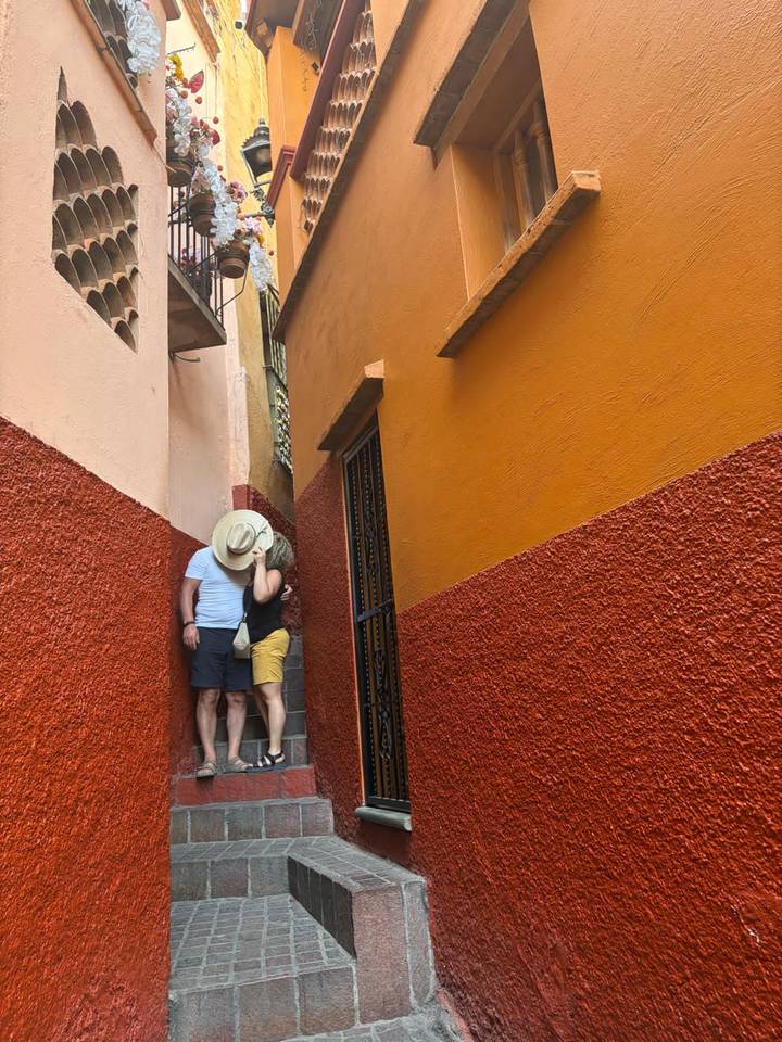 Couple sharing a kiss in a narrow brightly painted alleyway with red and orange walls