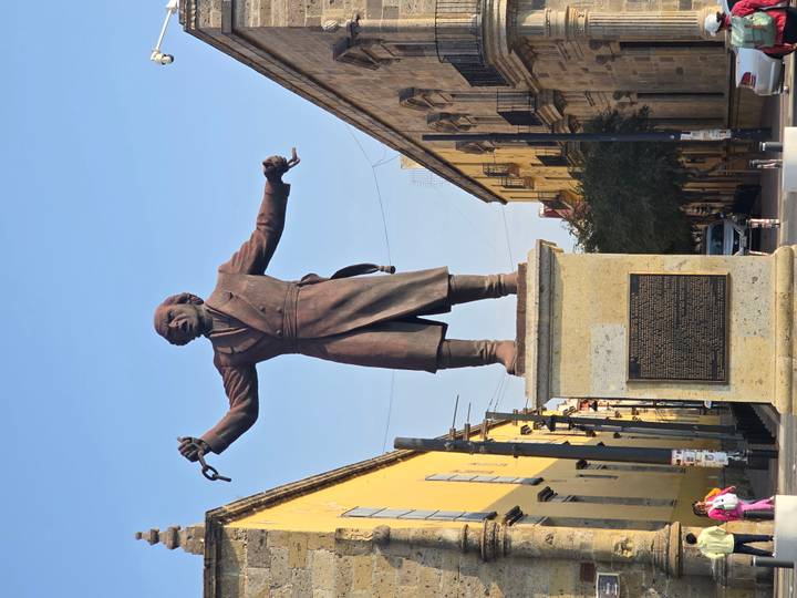 Tall bronze statue of a historical figure holding broken chains in a sunny plaza