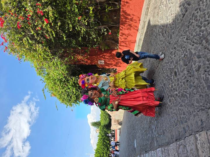 Two towering festival puppets in colorful dresses parade down a cobblestone street with a young boy