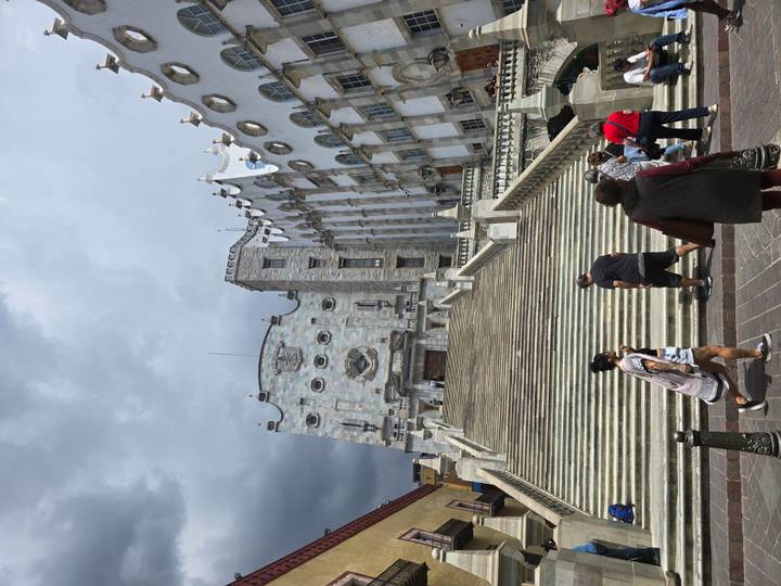 Visitors climb the grand staircase leading to the ornate façade of the University of Guanajuato under dramatic skies