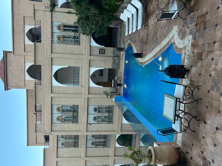 Elegant riad courtyard featuring arched balconies and a turquoise mosaic swimming pool.
