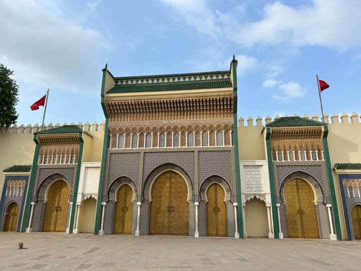 Intricate golden gates and green-tiled towers of the Royal Palace in Fes against a blue sky.