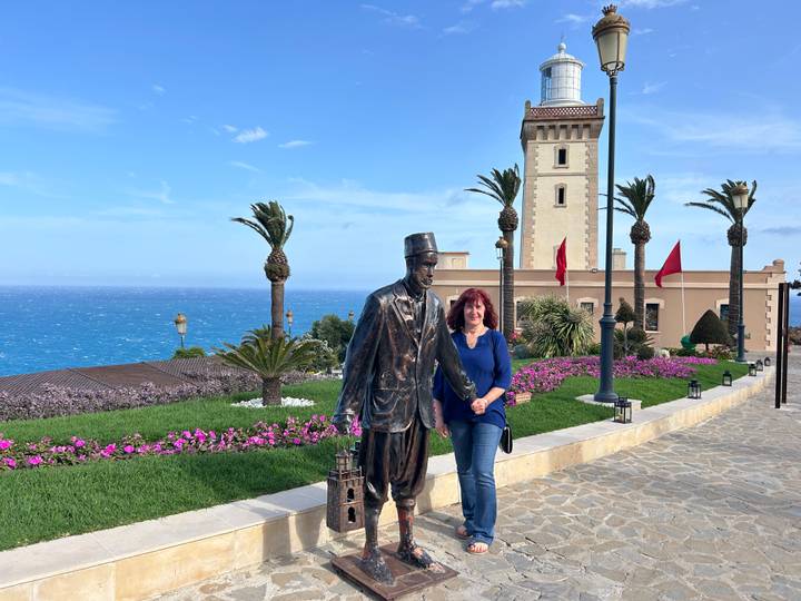 Traveler poses beside bronze statue near a lighthouse overlooking the blue Atlantic in Tangier.