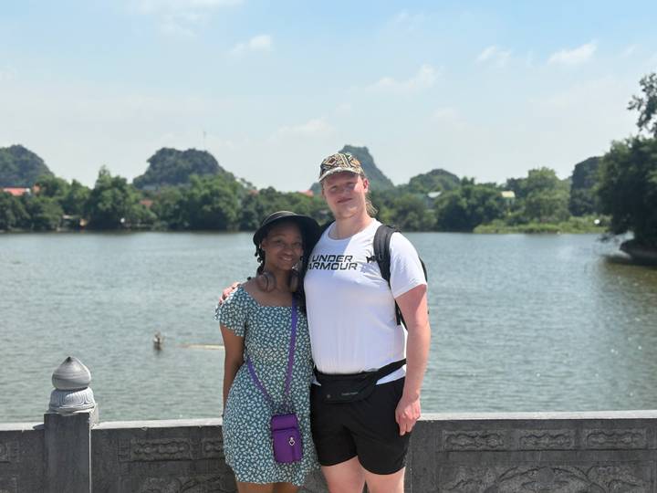 Couple poses by a tranquil lake with karst hills of Ninh Binh in the background.