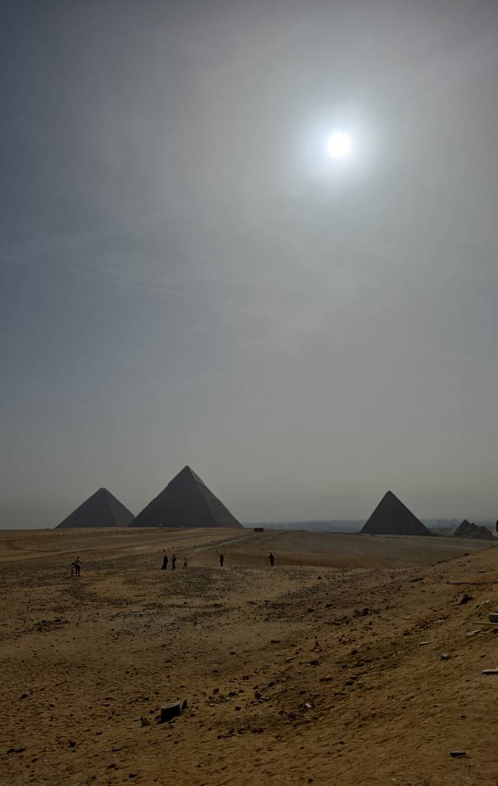 Distant silhouette of three pyramids under a hazy, overexposed sky