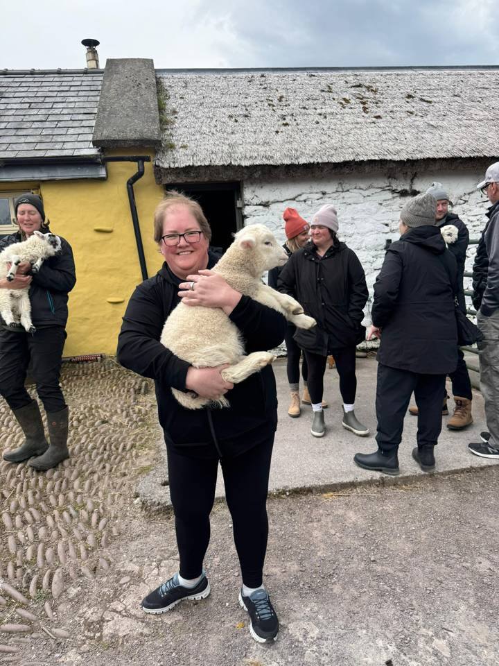 Traveller holding a lamb while others gather at a rural Irish farmstead.