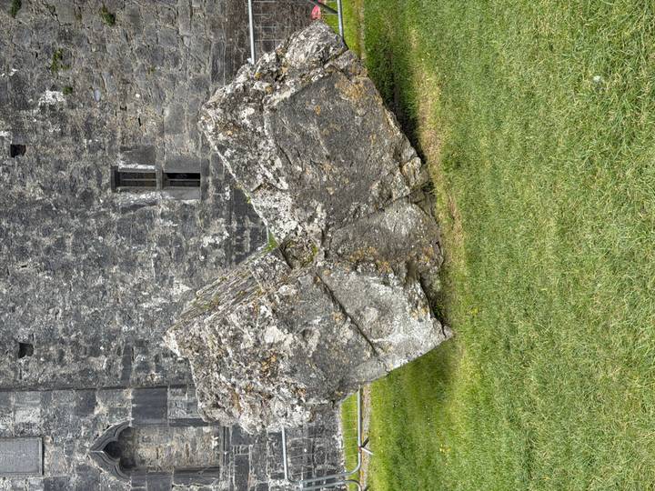Massive irregular stone block displayed on the lawn of a historic Irish castle.