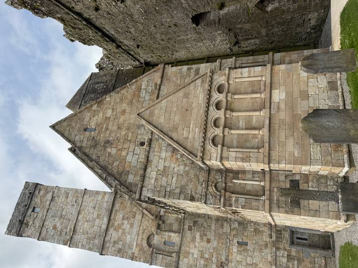 Stone church side wall with Romanesque arches and gravestones in foreground.