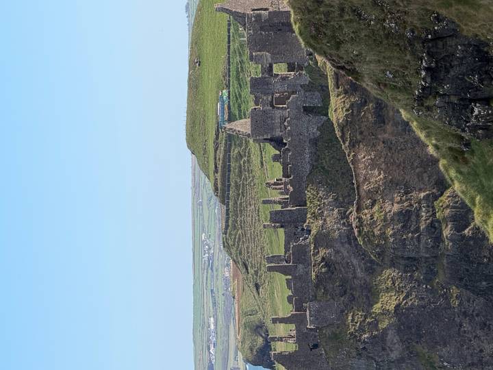 The dramatic cliff-top ruins of Dunluce Castle overlook the green Antrim coastline under a clear blue sky.