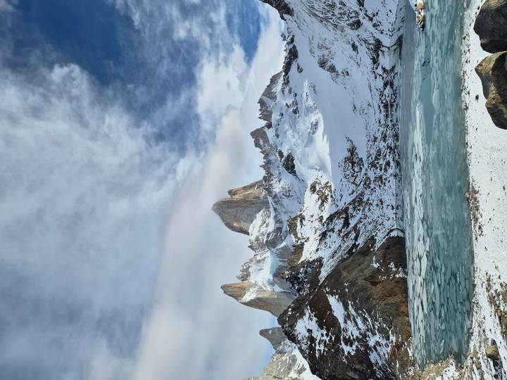 Snow-clad Mount Fitz Roy rises dramatically above a frozen turquoise lagoon under patchy clouds.