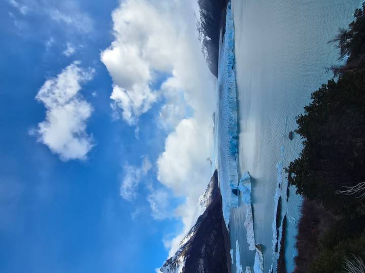 The vast Perito Moreno Glacier extends across a milky blue lake beneath dynamic clouds.