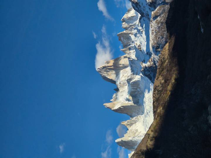 Sharp granite peaks of Mount Fitz Roy gleam against a deep blue sky, their lower slopes dusted with snow.