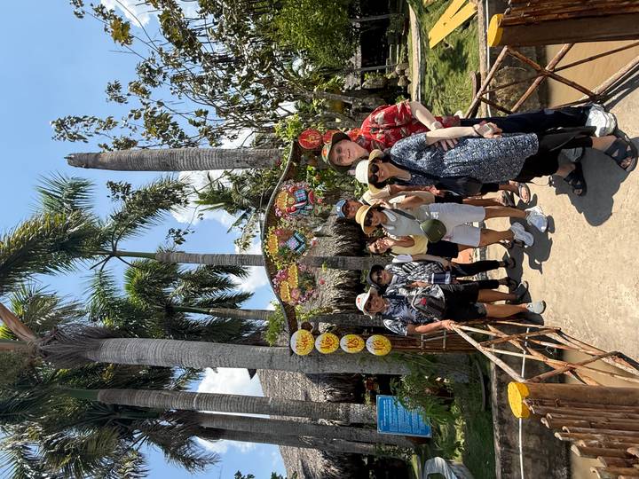 Travellers smile beneath a decorated arch at a riverside garden attraction in the Mekong Delta.