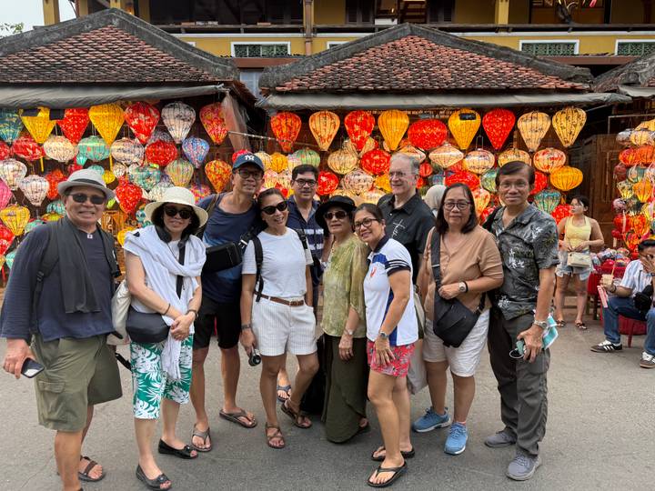 A group of tourists stand in front of colourful hanging lanterns in Hoi An’s old town market.