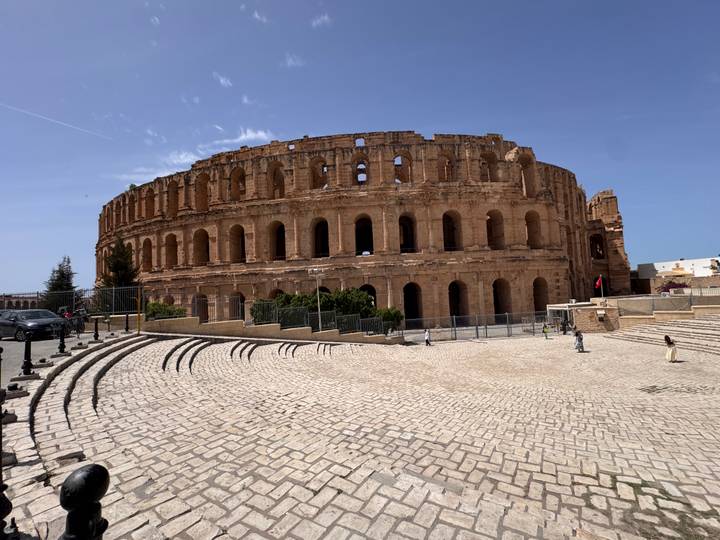 The grand Roman amphitheatre of El Jem dominates the plaza under a clear blue sky.