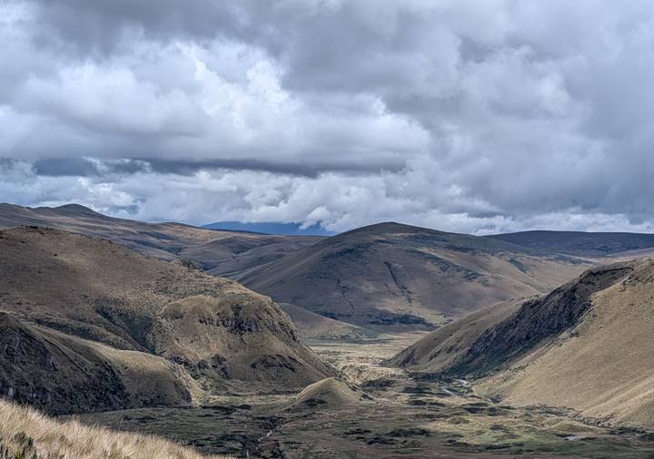 Rolling Andean highlands under dramatic clouds with a remote valley floor and rugged ridges.