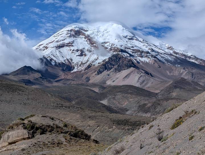 The snow-capped cone of Chimborazo Volcano towers above dry Andean plains and rocky foothills.