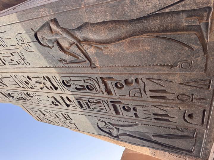 Granite obelisk surface carved with deep hieroglyphs and relief of pharaoh holding offering.