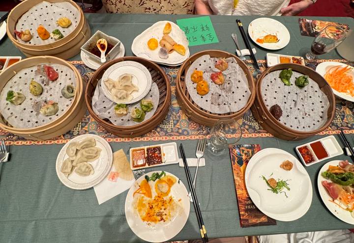Overhead view of a banquet table with colorful dumplings, dipping sauces and chopsticks arranged on bamboo steamers.