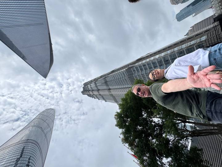 Up-angle shot of a couple reaching toward the camera with Shanghai’s soaring skyscrapers and dramatic clouds above.