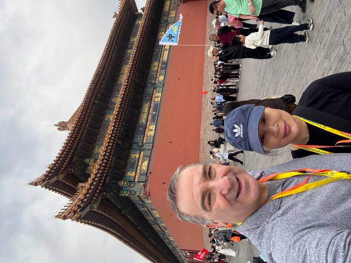 Couple taking a selfie near a richly decorated corner tower in Beijing’s Forbidden City with tourists in the background.