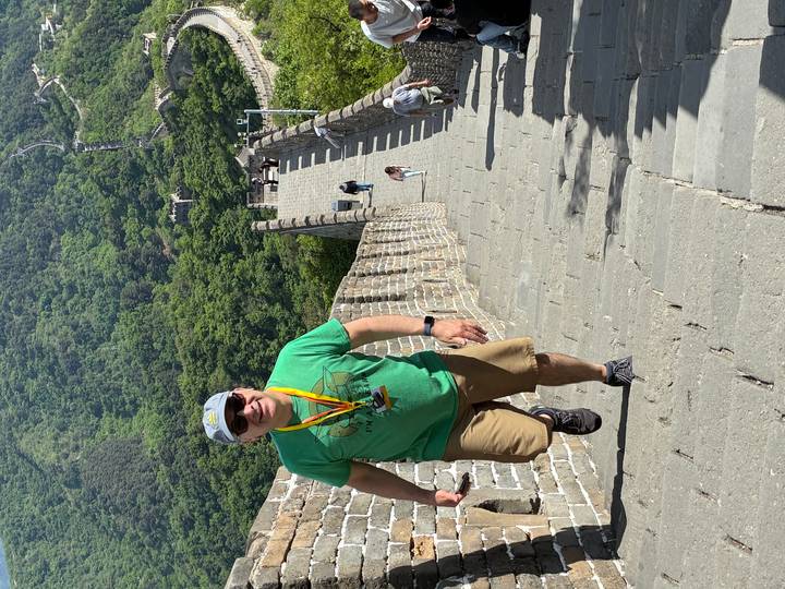Traveler climbing a steep stone stairway on the Great Wall of China surrounded by lush green hills.