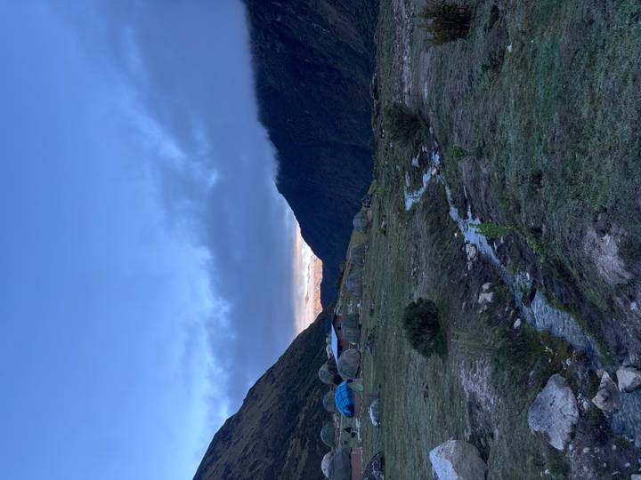 Remote campsite domes beneath misty ridges and a blue twilight sky with a trickling stream in foreground